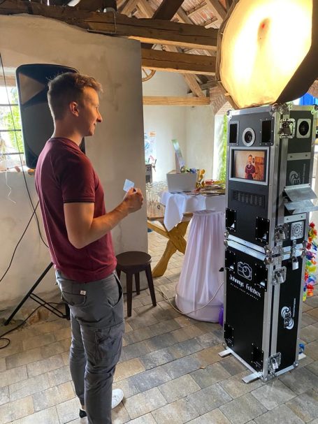 Ein Mann steht neben einem Fotokabine in einem festlich dekorierten Raum.