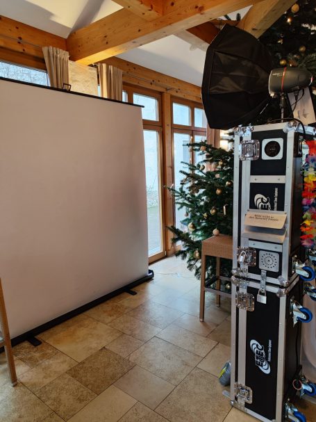 Leinwand vor einem Fenster, neben einem geschmückten Weihnachtsbaum und einem Equipmentschrank.